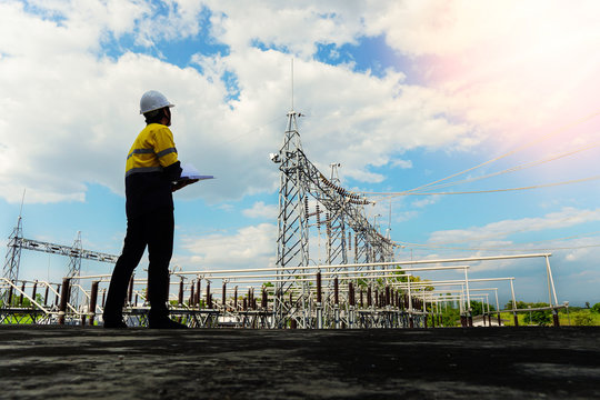 A low-angle view of the engineer looking at the drawing of a small size power plant to verify installation accuracy to meet standards. The background is the structure of the power plant with blue sky