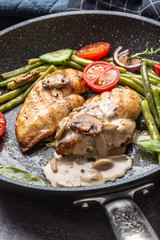 Portrait close up of a grilled chicken fillet with a creamy mushrooms sauce, green beans and tomatoes in a skillet