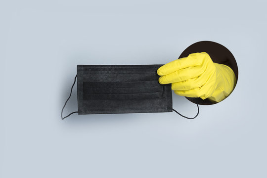 Coronavirus prevention medical black mask in protective yellow gloves in hand through paper hole. COVID-19.