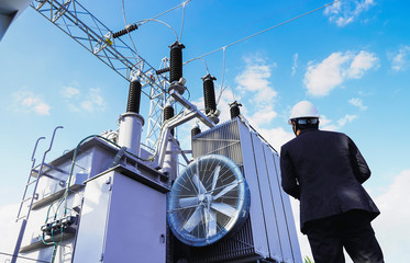 A low angle image of a businessman wearing a black suit, standing looking at a large power...