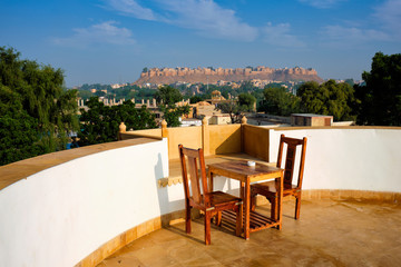 Fototapeta na wymiar Rooftop Table with chairs with view of tourist landmark of Rajasthan - Jaisalmer Fort known as the Golden Fort Sonar quila, Jaisalmer, Rajasthan, India