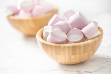 Pink and white marshmallows in a full wooden bowls placed on a marble surface with a focus on the bowl in the front