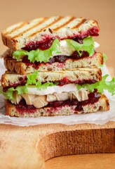 Delicious Turkey or chicken sandwich with brie or Camembert cheese, lettuce and cranberry (lingonberry, cowberry) chutney on grain bread with flax seed. Gourmet Breakfast. Panini. Selective focus