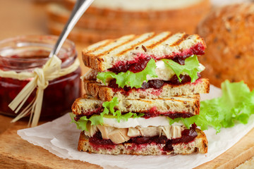 Delicious Turkey or chicken sandwich with brie or Camembert cheese, lettuce and cranberry (lingonberry, cowberry) chutney on grain bread with flax seed. Gourmet Breakfast. Panini. Selective focus