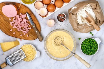 Preparation of dough for homemade Savory muffins for Breakfast. Ingredients on the marble table - wheat flour, eggs, butter, sausage or ham, Parmesan cheese, green peas and spices salt and pepper