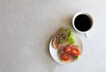 Plate with tapas meat filling, lettuce, microgreens and tomatoes, a cup of hot aromatic coffee on a gray background, copy space, flat lay