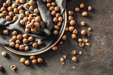 Top view of hazelnuts and their cracked shells on a rustic dark metallic background, in a metallic cup and on a tray
