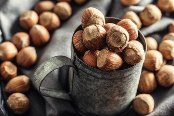 Close up of a vintage metallic mug full of hazelnuts with more nuts on a textile table cloth around it