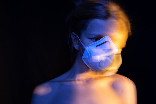 Scared woman portrait in white respirator. personal protection.  polluted air by respiratory diseases. ecological problems. post apocalypse. Long exposure creative series of photos. Black blue orange