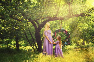 Obraz na płótnie Canvas fashion outdoor photo of beautiful family look. beautiful mother with long blonde hair posing and playing with her daughter in similar lavender dresses in the park outdoor