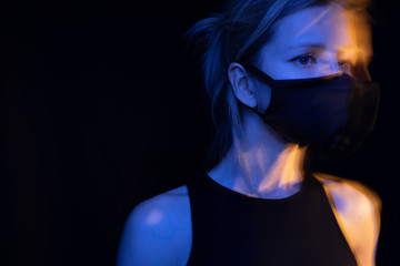 Face mask protects against virus and respiratory infections. Young slim woman black background in blue and orange colors. Long exposure conceptual photos. tense anxious look. quarantine Sad emotions 