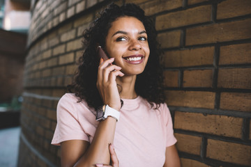 Happy dark skinned hipster girl smiling during positive friendly smartphone conversation, cheerful African American teenage woman enjoying free time for communication via cellphone application