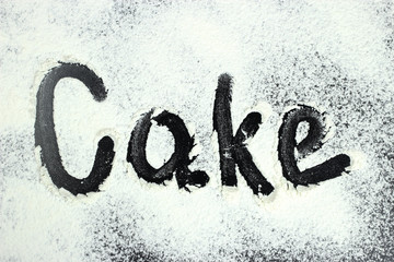The word cake is drawn with finger on flour, white powder