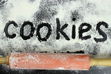 The word cookies is drawn with finger on the flour and rolling pin