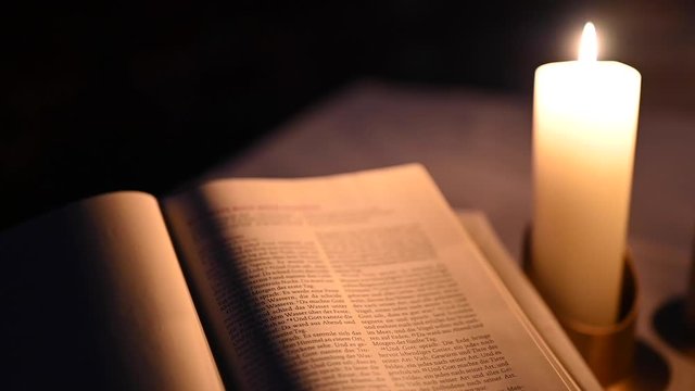 Holy Bible With White Candles In The Dark. Camera pans from left to right.