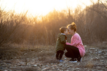 Beautiful mother playing with her son in nature against sunset. Mother's day concept