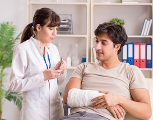 Obraz premium Young man with bandaged arm visiting female doctor traumatologis