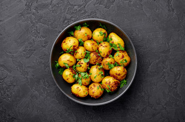 Jeera Aloo in black bowl on dark slate background. Jeera Aloo is indian cuisine dish with baby potatoes, jeera seeds and coriander. Copy space