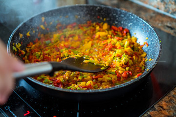 Person stirring a pan with colorful vegetables over a slow fire with a kitchen utensil. Food lovers.