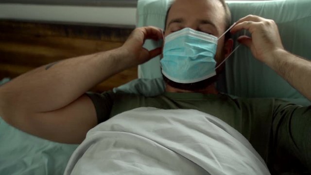 Man laying in bed being sick wearing surgical mask