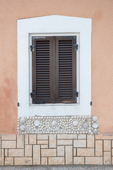 window with closed brown shutters, white frame and shell decoration. mediterranean facade
