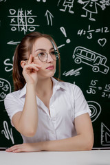 Fototapeta premium Young teacher is sitting near blackboard in classroom