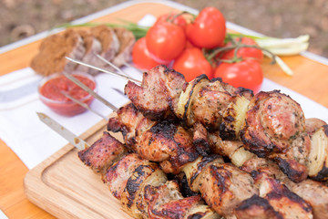 Pork shish kebabs on skewers with fresh vegetables, on a wooden background. Barbecuing lunch