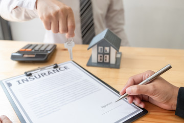 Real estate agent broker hand over the house key to the new owner after completing the signing according to agreement renting a house and buy house insurance Home insurance concept