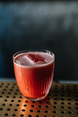 Whiskey sour cocktail with strawberry and red bell pepper smoothie decorated with pepper seeds. Cold blue color background.