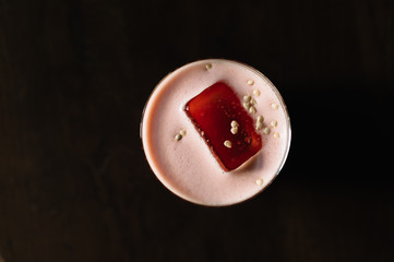 Whiskey sour cocktail with strawberry and red bell pepper smoothie decorated with pepper seeds.. Top view. Dark wooden table background.