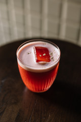 Whiskey sour cocktail with strawberry and red bell pepper smoothie decorated with pepper seeds.. White tiles wall and dark wooden table as a background.