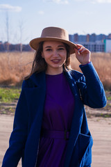 Young girl with beige hat and in blue coat walks early spring in field. Fashion, style, emotions.