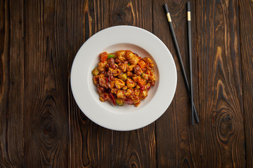 Chinese food, kung pao chicken in white plate with chopsticks on wooden table, top view and copy space