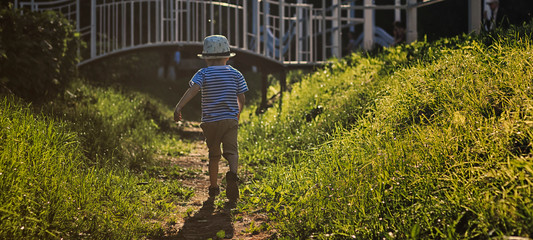 A small child a boy 2 - 3 - 4 years old runs along a path in a sunny park to the bridge. The concept of summertime, childhood and independence of the child.