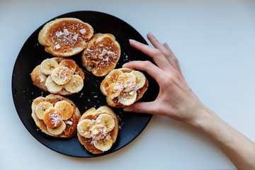 Hand is holding homemade fruit banana cake for breakfast on the black ceramic plate. Top view. selective Focus