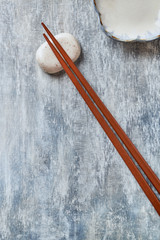 Wooden chopsticks and chopstick rest on rustic wooden background. Top view. Copy space.