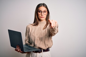 Young beautiful brunette woman working using laptop over isolated white background pointing with finger to the camera and to you, hand sign, positive and confident gesture from the front