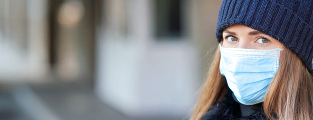 Young woman wearing disposable blue virus face mouth nose mask, closeup portrait - wide banner with space for text left side. Coronavirus covid-19 outbreak prevention concept