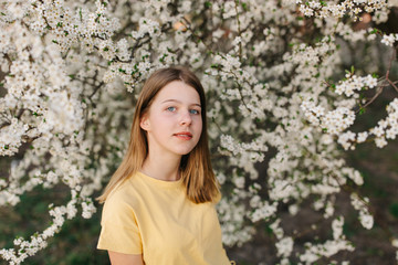 portrait of sad young woman in protective medical face mask with flowers near blooming tree in spring time. Coronavirus protection. epidemic of coronavirus. the aroma a tree in the garden on a spring