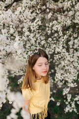 portrait of sad young woman in protective medical face mask with flowers near blooming tree in spring time. Coronavirus protection. epidemic of coronavirus. the aroma a tree in the garden on a spring