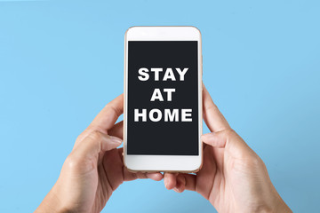 Hands holding a mobile phone with a message for Stay at home on the screen