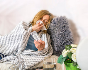 Ill sick woman lies in bed blowing her nose, coughing and drinking pills. Concept diseases of flu virus, colds, seasonal allergies, coronavirus