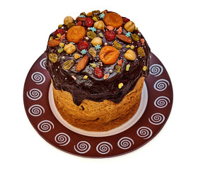 Sweet Easter cake poured with chocolate and decorated with dried fruits from dried apricots, candied fruits, cherries, raisins and also hazelnuts, almonds and seeds isolated on a white background