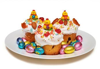 Sweet easter cakes in white protein glaze, decorated with dried fruits and nuts and a yellow chicken on a round plate isolated on a white background