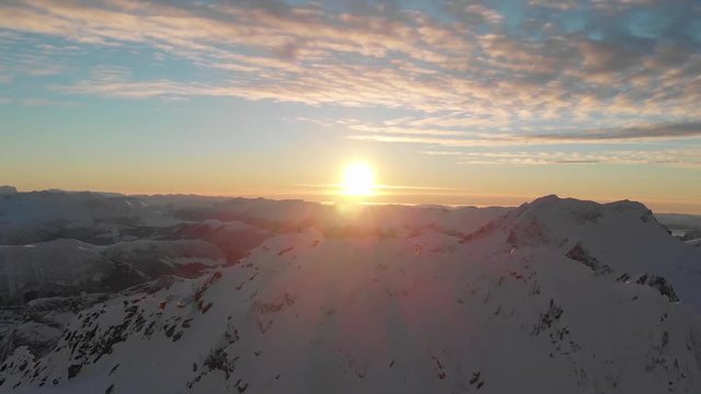 Person standing on summit as the sun is laying low on the sky. Drone shoot of mountains.