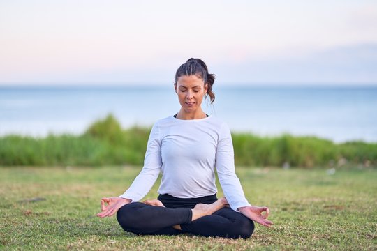 Young beautiful sportwoman practicing yoga. Coach sitting teaching lotus pose at park