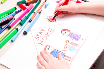 the child draws with felt-tip pens a family and a house on paper, felt-tip pens on the table, the inscription in the picture stay home, quarantine concept, self-isolation with the child