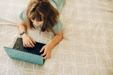 indoor portrait of child girl with laptop lying on bed at home