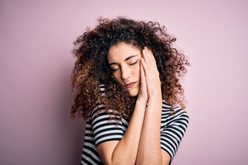 Young beautiful woman with curly hair and piercing wearing casual striped t-shirt sleeping tired...