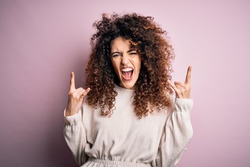Beautiful woman with curly hair and piercing wearing casual sweater over pink background shouting...